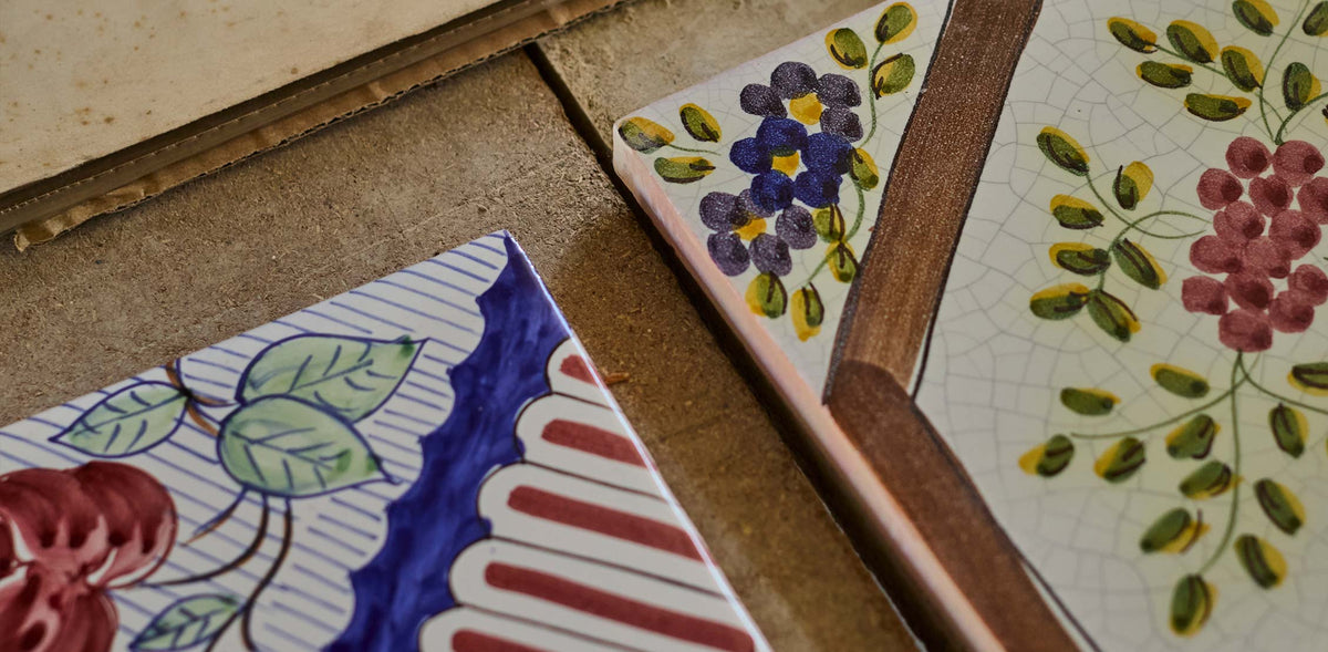 Decorative ceramic tiles with hand-painted floral and striped patterns, arranged on a rustic wooden surface.